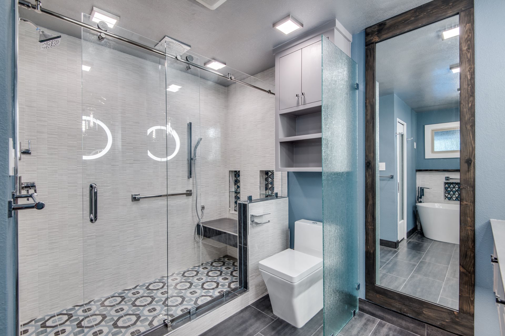 A bathroom remodel with a toilet , shower , sink and mirror.
