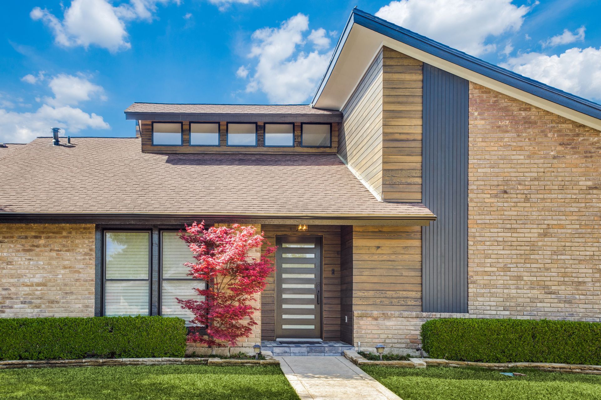 A brick house with a blue roof and a tree in front of it.