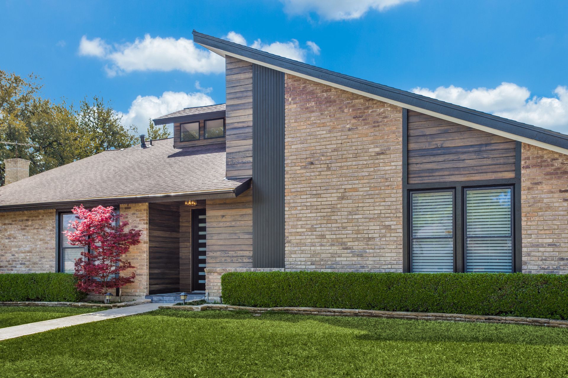 A brick house with a sloped roof and a lush green lawn.