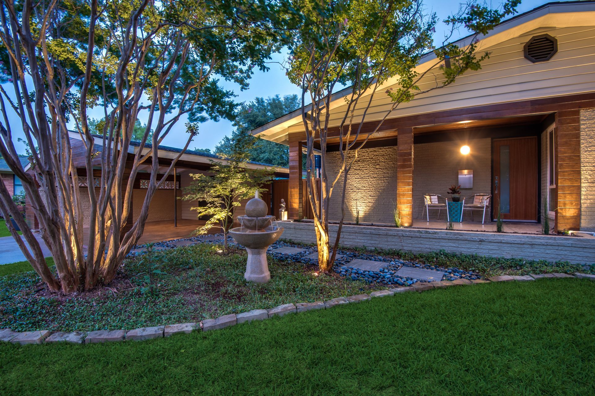 A house remodel with a lush green lawn and trees in front of it.