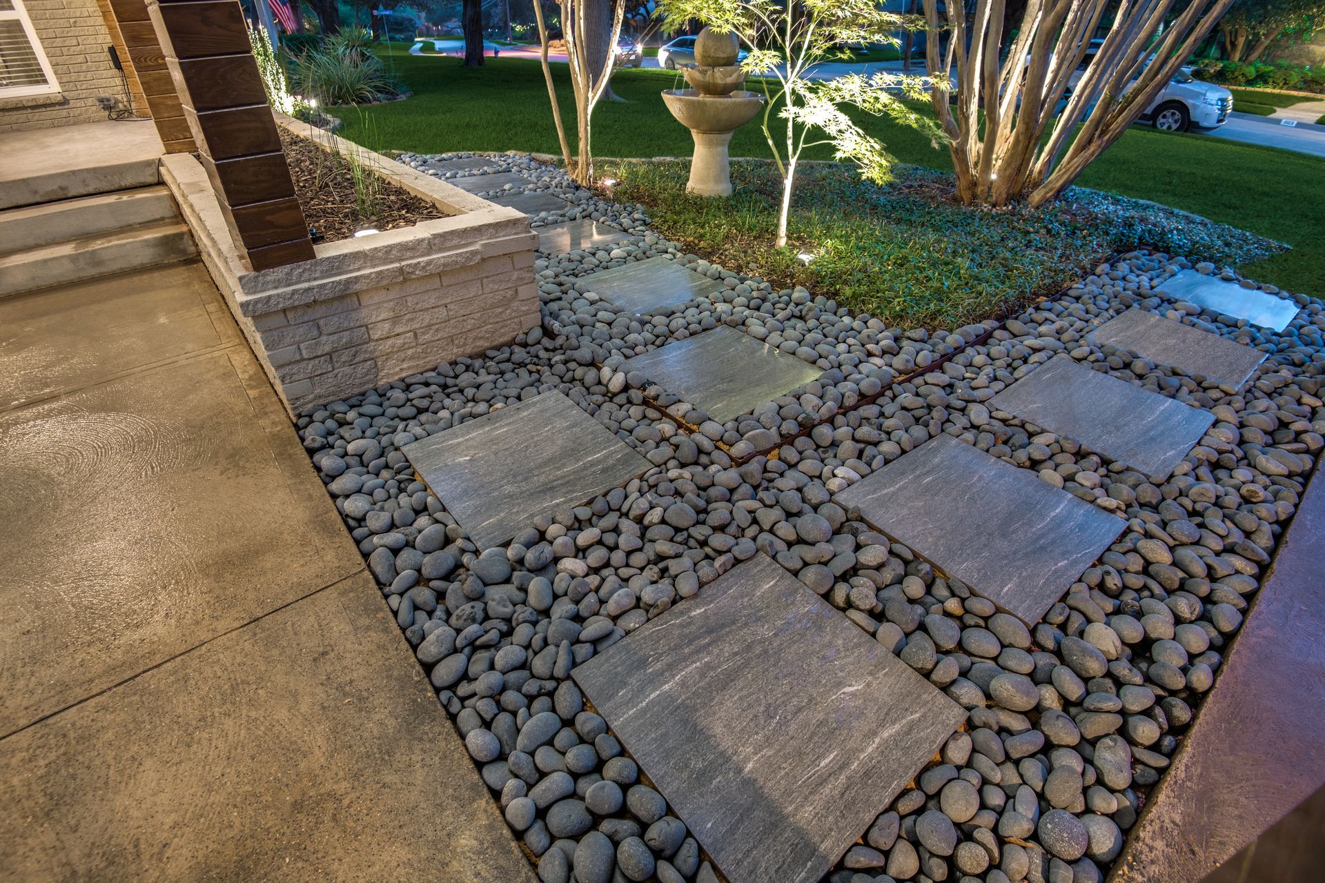A stone walkway leading to a house with a fountain in the background.