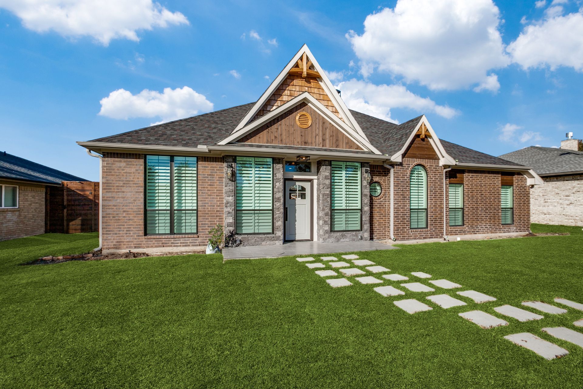 A large brick house remodel with a lush green lawn in front of it.