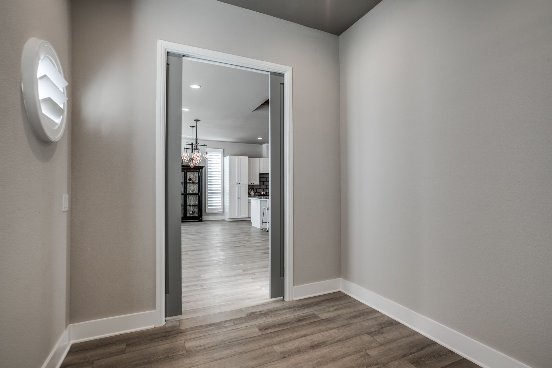 An empty room with hardwood floors and a sliding door leading to a kitchen.