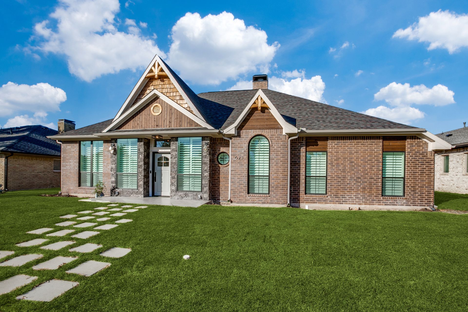 A large brick house remodel with a lot of windows is sitting on top of a lush green lawn.