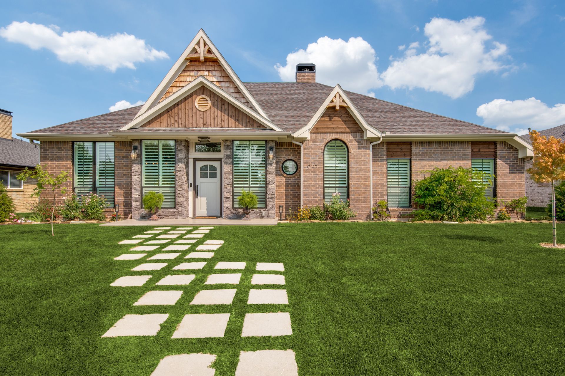 A large brick house remodel with a lush green lawn and a stone walkway leading to it.