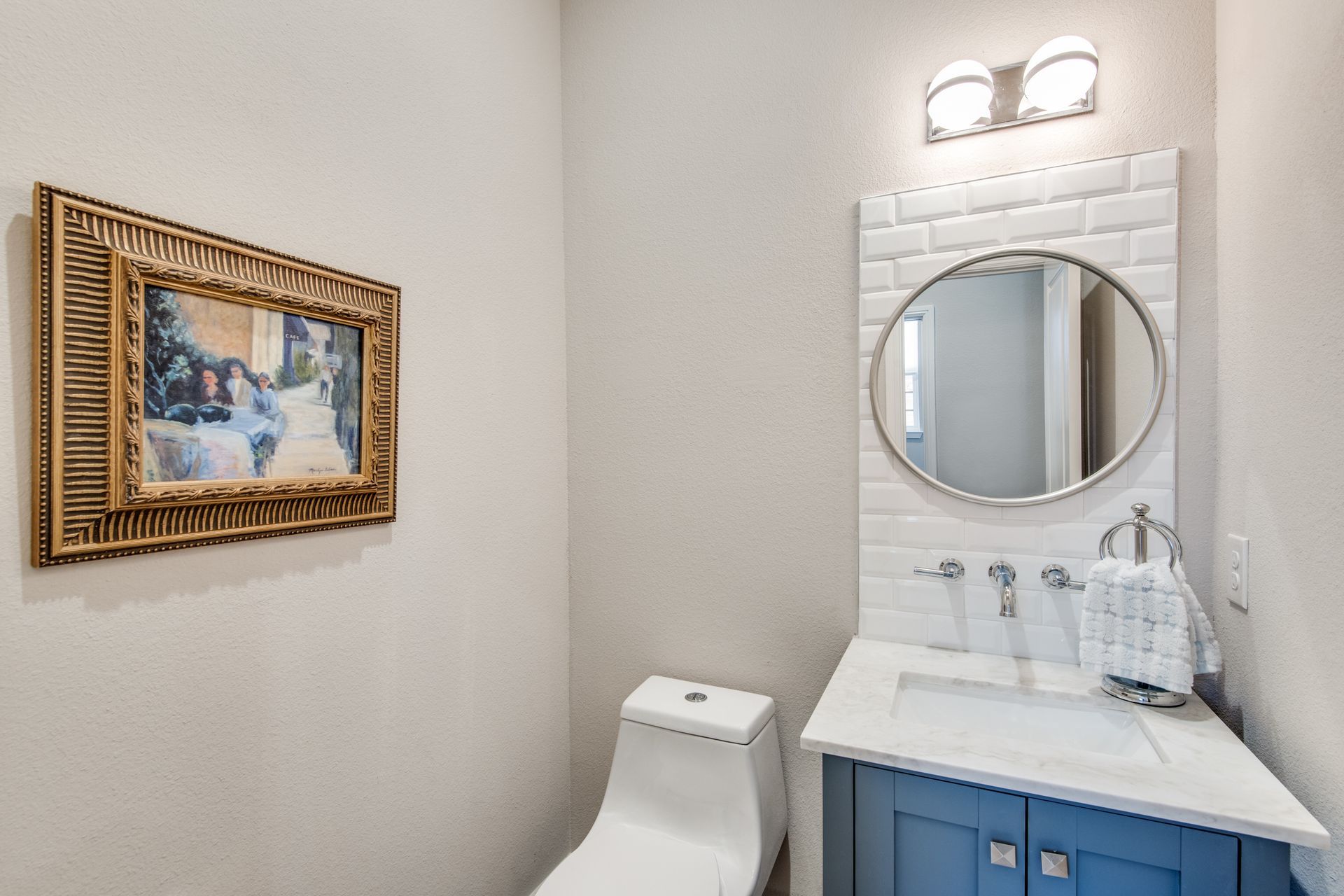A bathroom with a toilet , sink , mirror and picture on the wall.