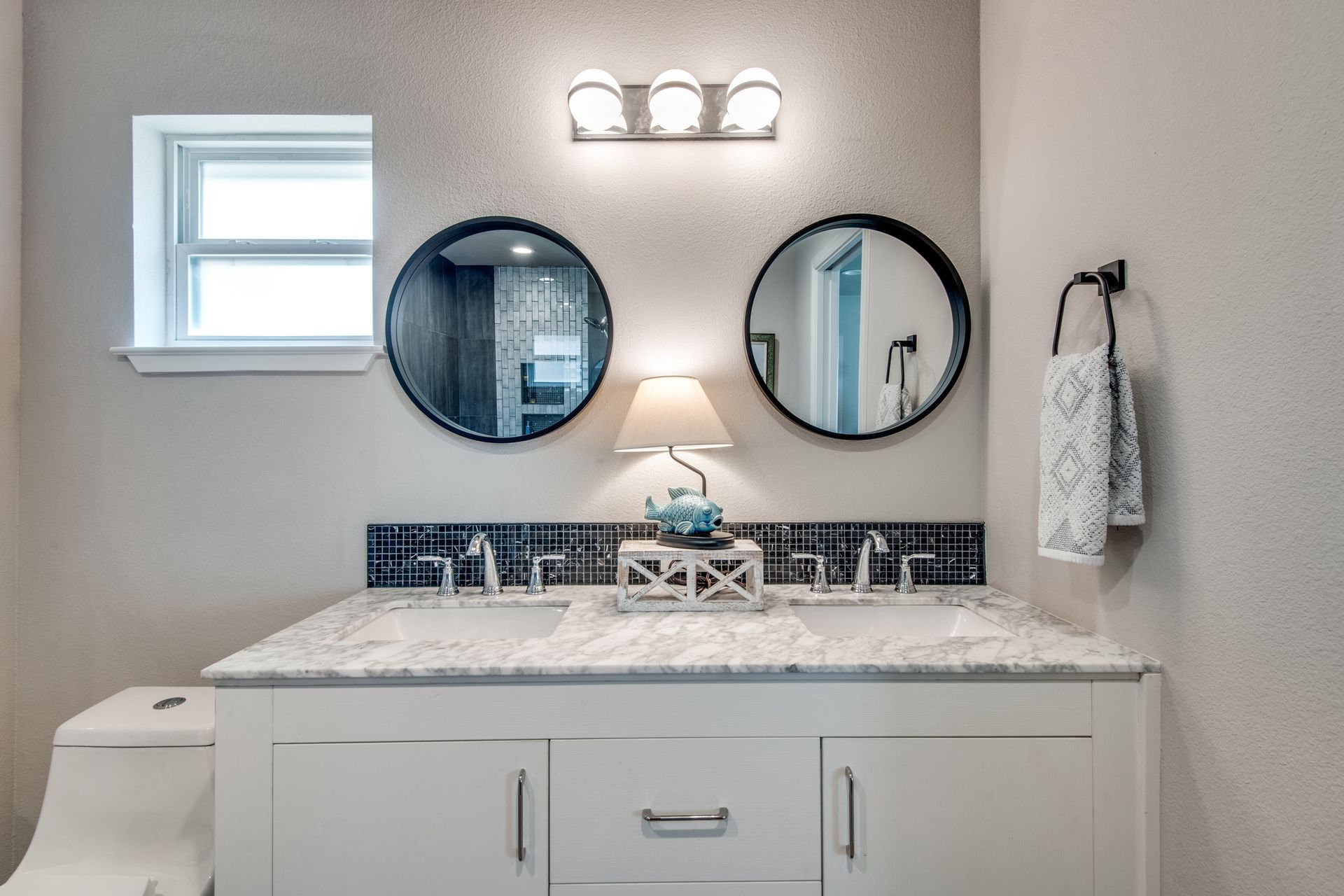 A bathroom with two sinks , two mirrors , a toilet and a window.