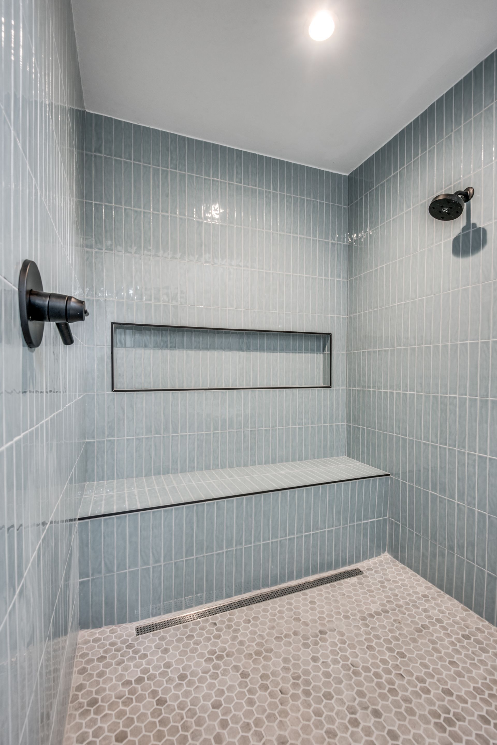 A walk in shower with blue tiles and a bench.