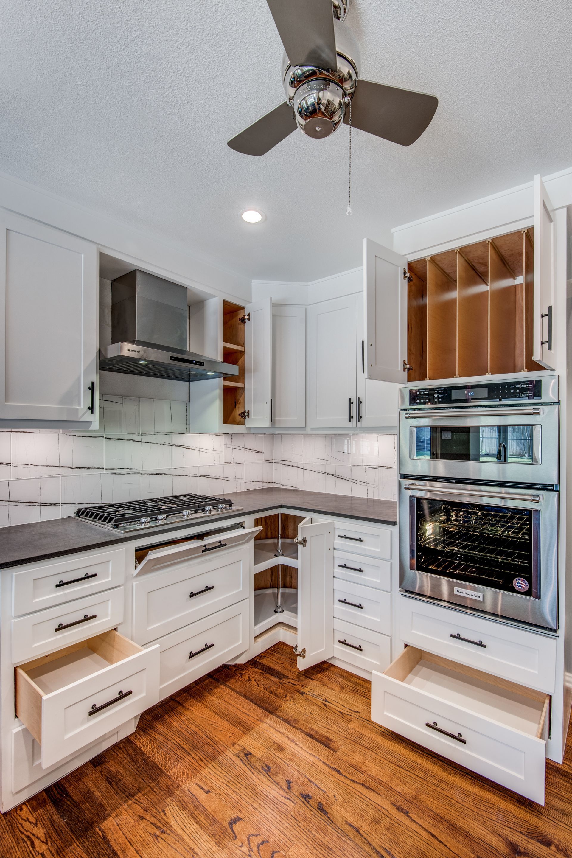 A kitchen with white cabinets , stainless steel appliances and a ceiling fan.
