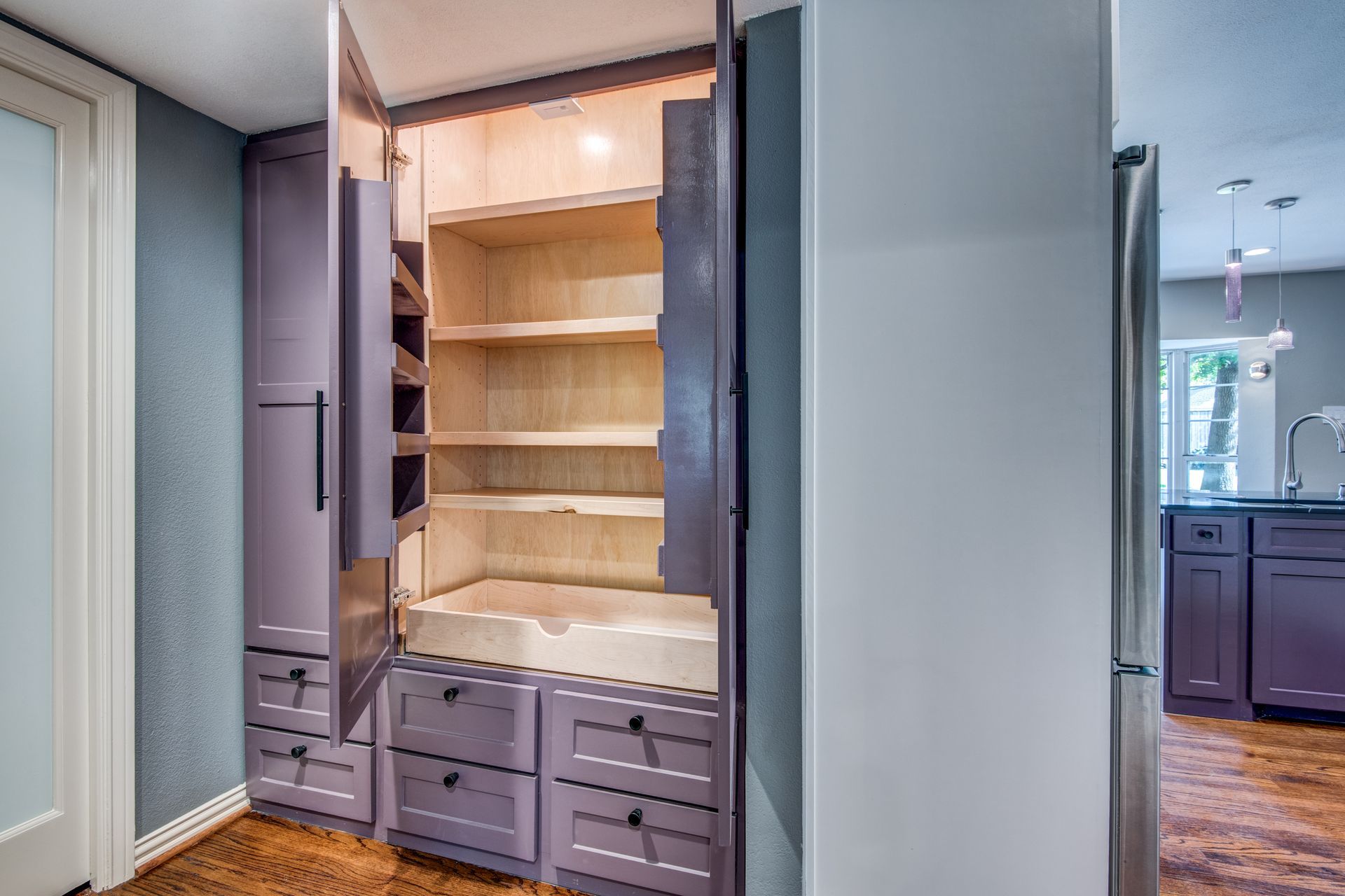 A purple pantry with its doors open in a kitchen.