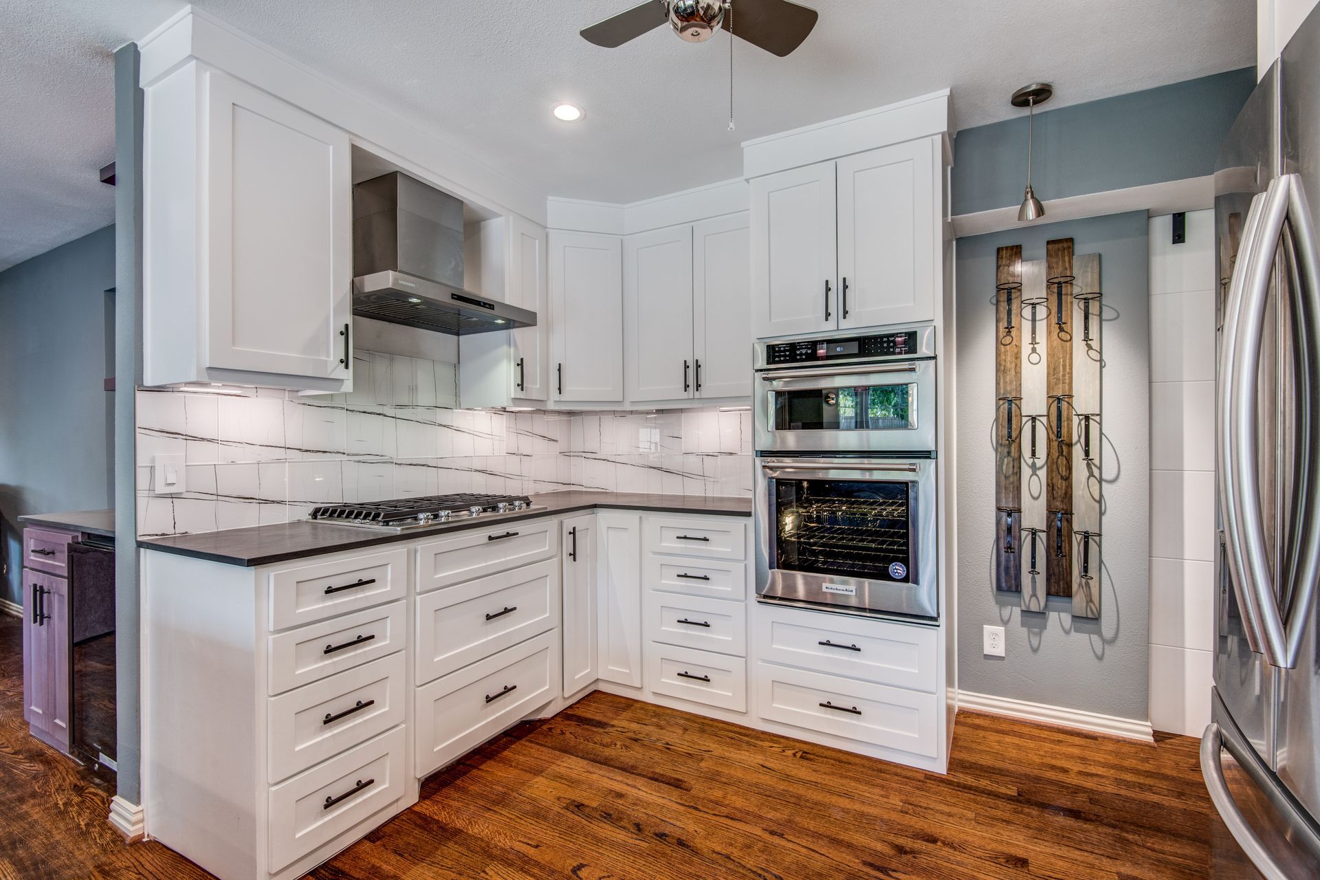 A kitchen with white cabinets , stainless steel appliances , hardwood floors and a ceiling fan.