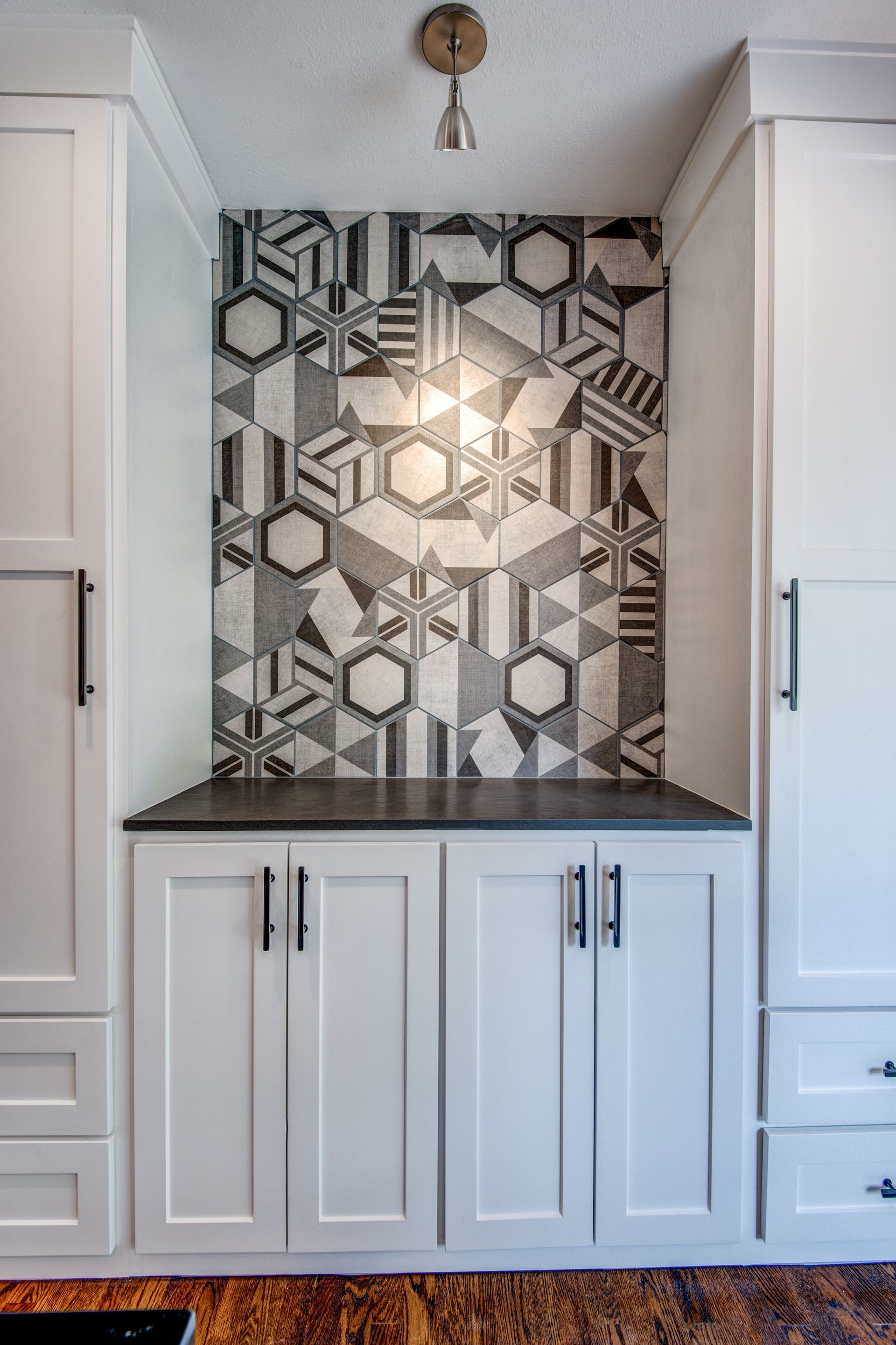 A kitchen with white cabinets and a black and white tile wall.