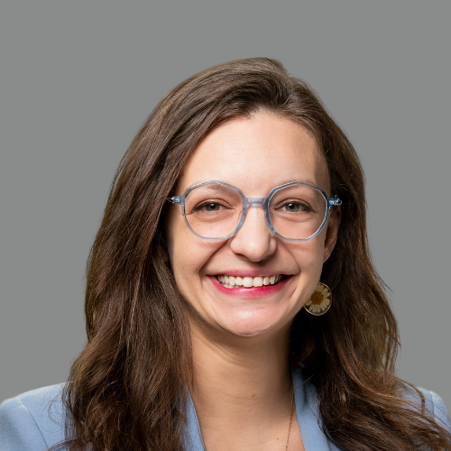 A woman wearing glasses and earrings is smiling for the camera.