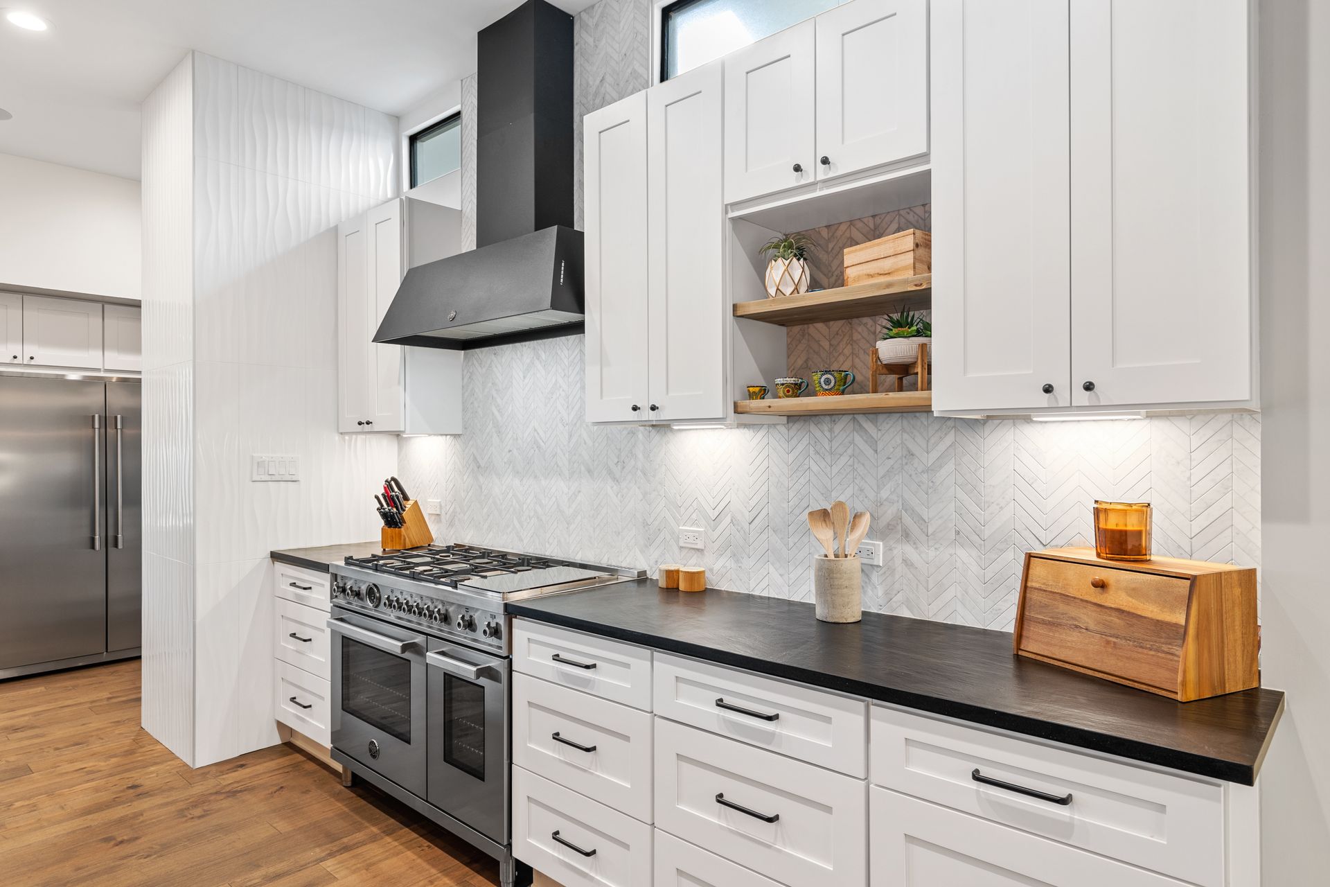 A kitchen with white cabinets , black counter tops , a stove and a refrigerator.