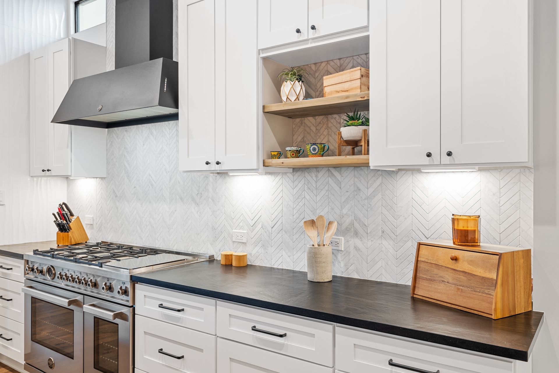 A kitchen with white cabinets , black counter tops , stainless steel appliances and a stove.