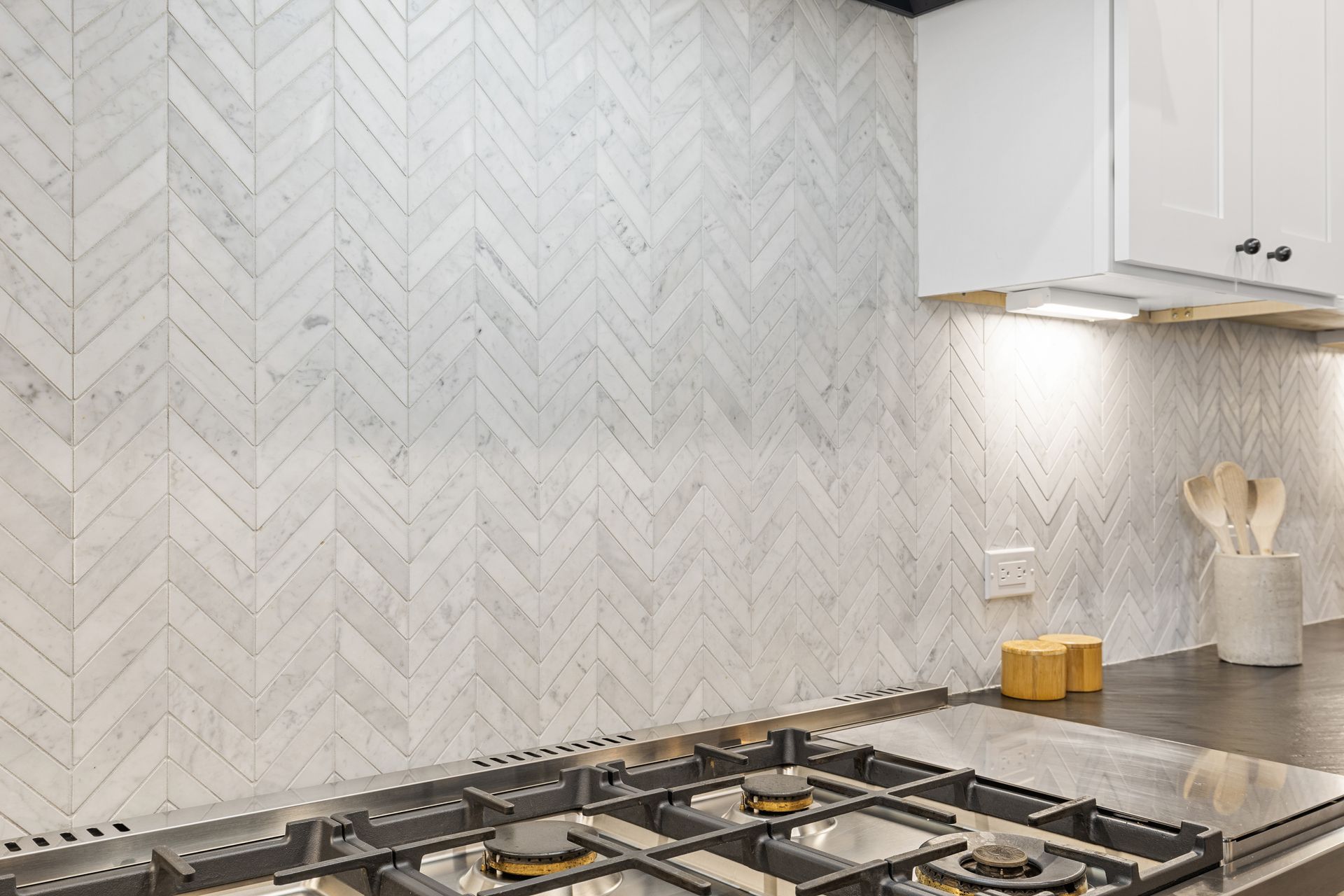 A kitchen with a stove top oven and a herringbone tile wall.