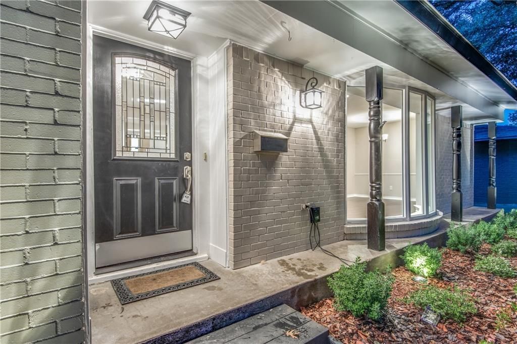 The front door of a house remodel with a brick wall and a black door.