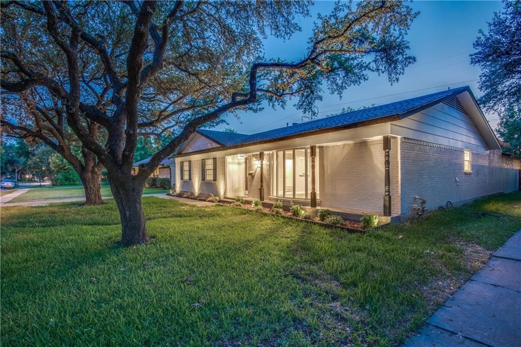 A house remodel with a porch and trees in front of it is lit up at night.