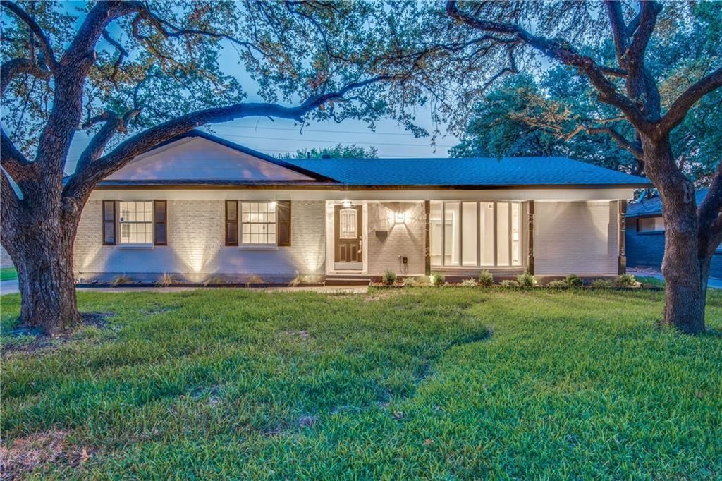 A large white house remodel is sitting on top of a lush green field.