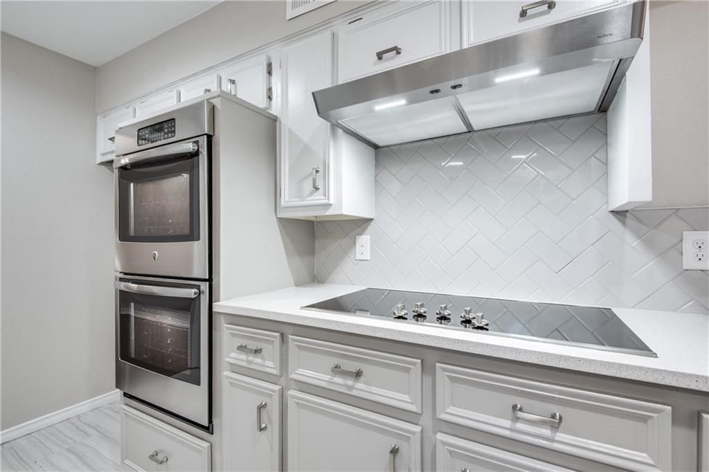 A kitchen with white cabinets , stainless steel appliances and a stove top oven.
