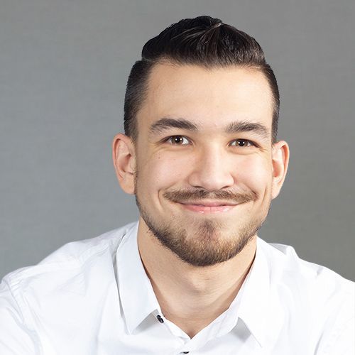 A man with a beard is smiling for the camera while wearing a white shirt.