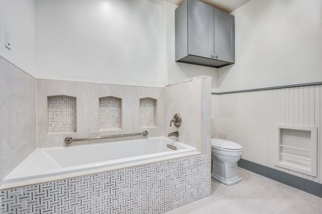 A bathroom with a bathtub , toilet and cabinets.