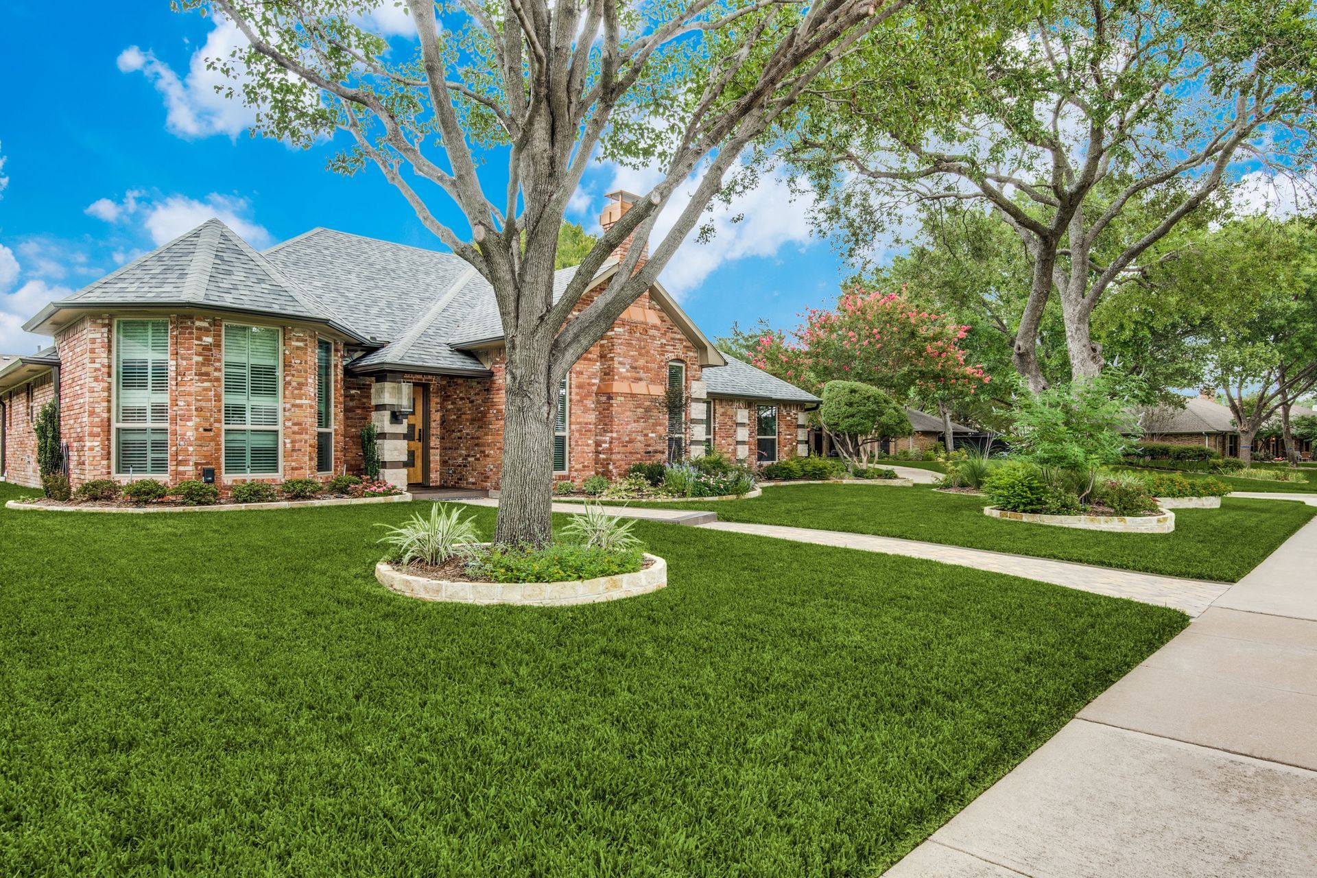 A brick house with a lush green lawn and trees in front of it.