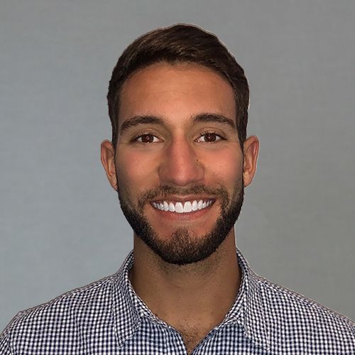 A man with a beard is smiling for the camera while wearing a plaid shirt.