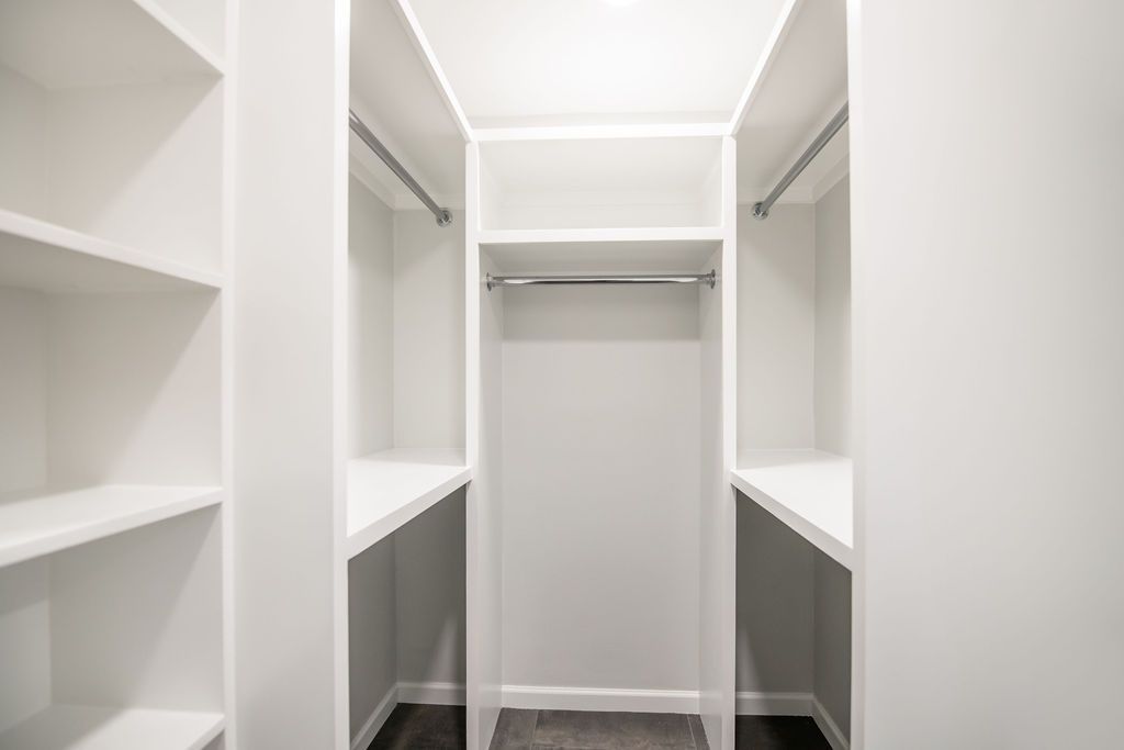 An empty walk in closet with white shelves and clothes racks.