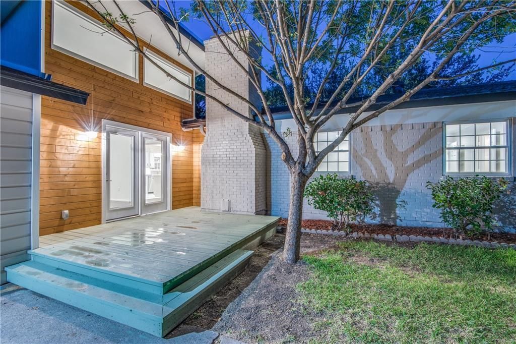 A house remodel with a deck and a tree in front of it.