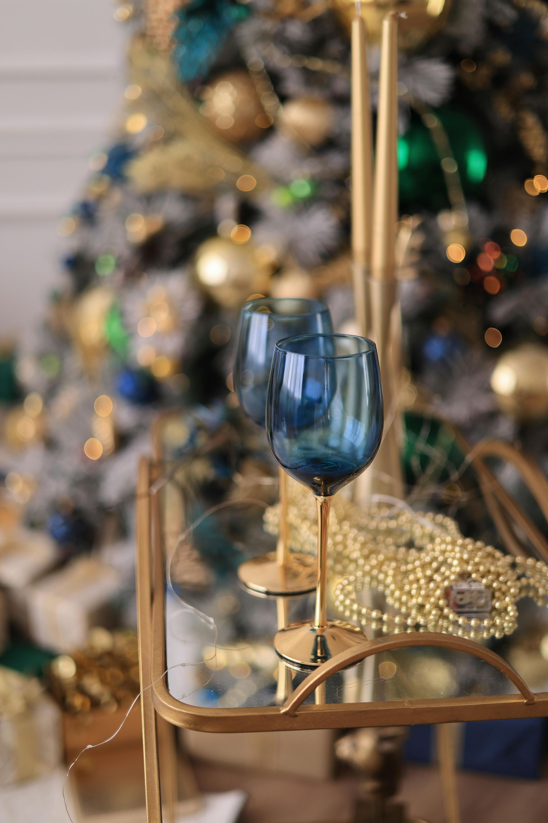Two blue wine glasses are sitting on a glass table in front of a christmas tree.