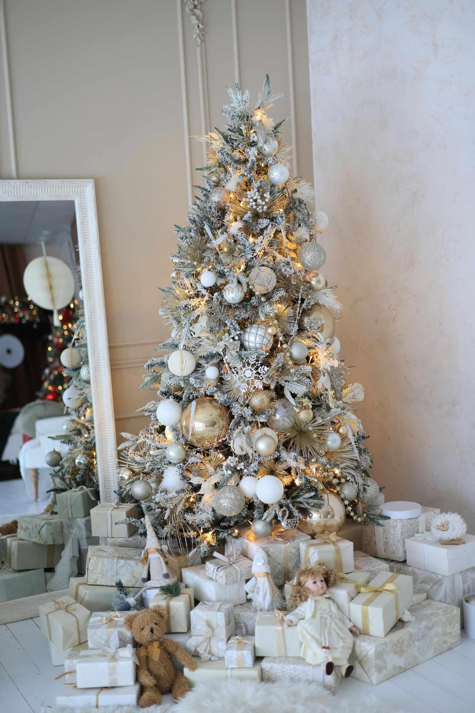 A christmas tree decorated in white and gold with gifts underneath it.