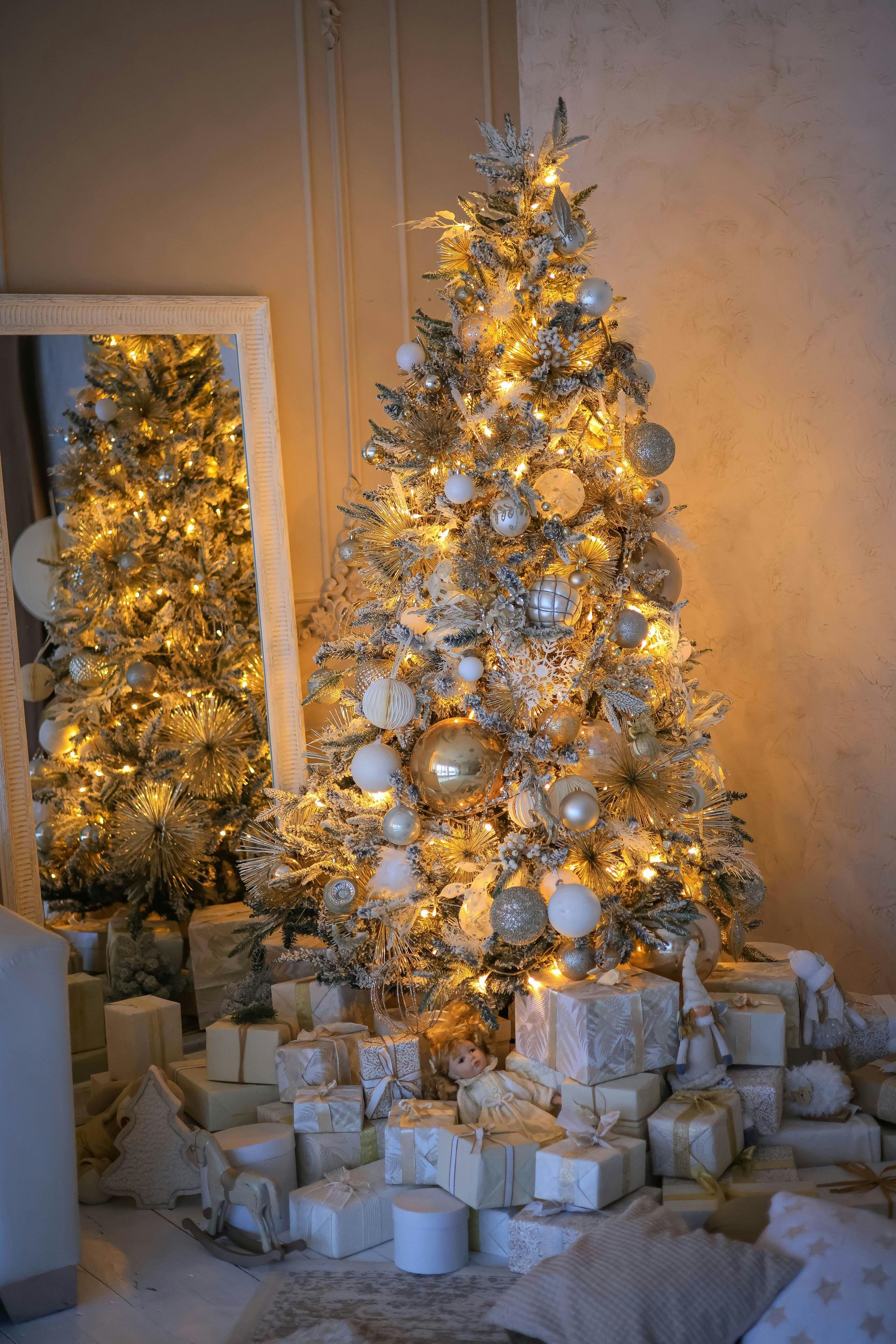 A christmas tree with gifts underneath it in front of a mirror.