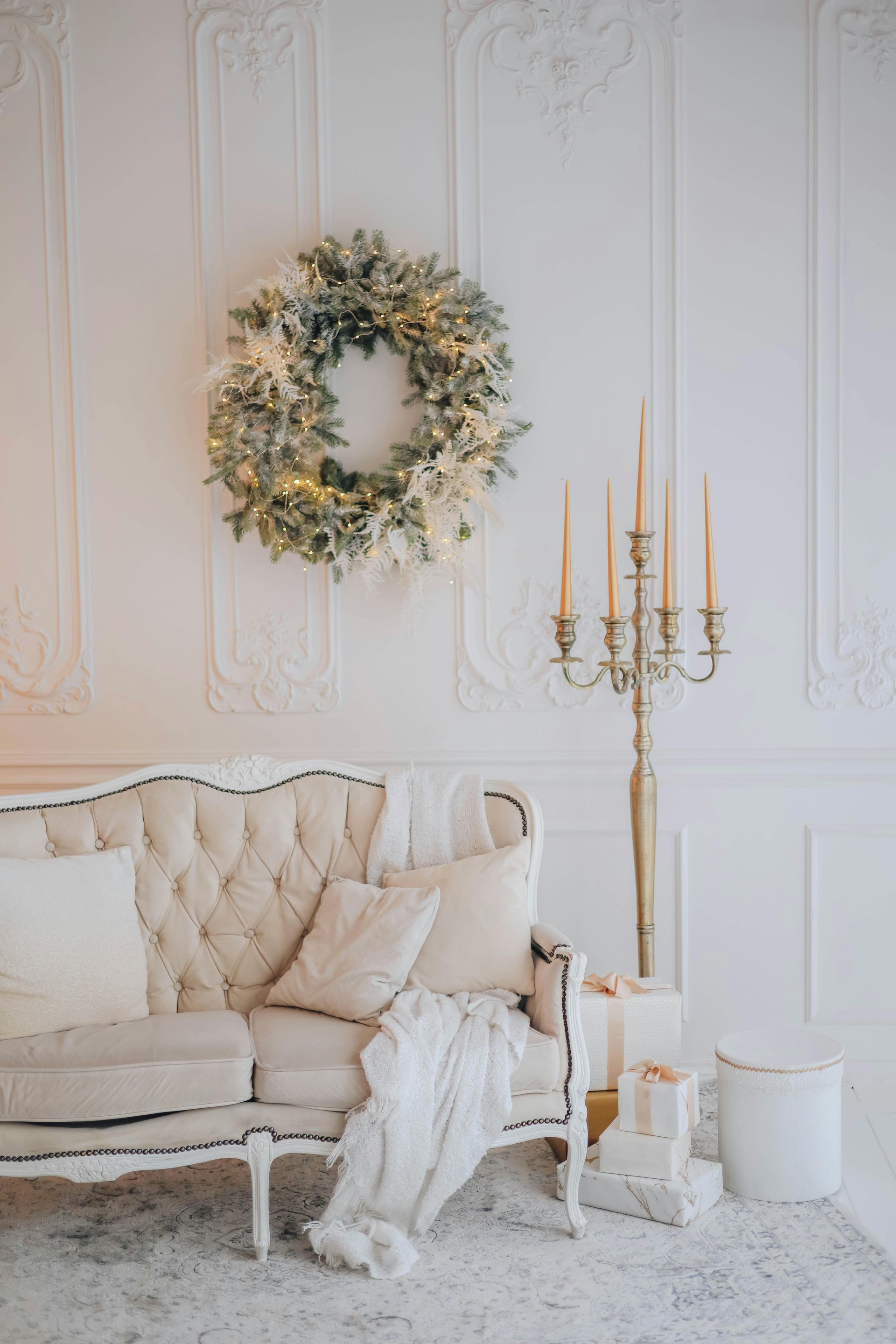 A living room with a couch , chair , candles and a wreath on the wall.