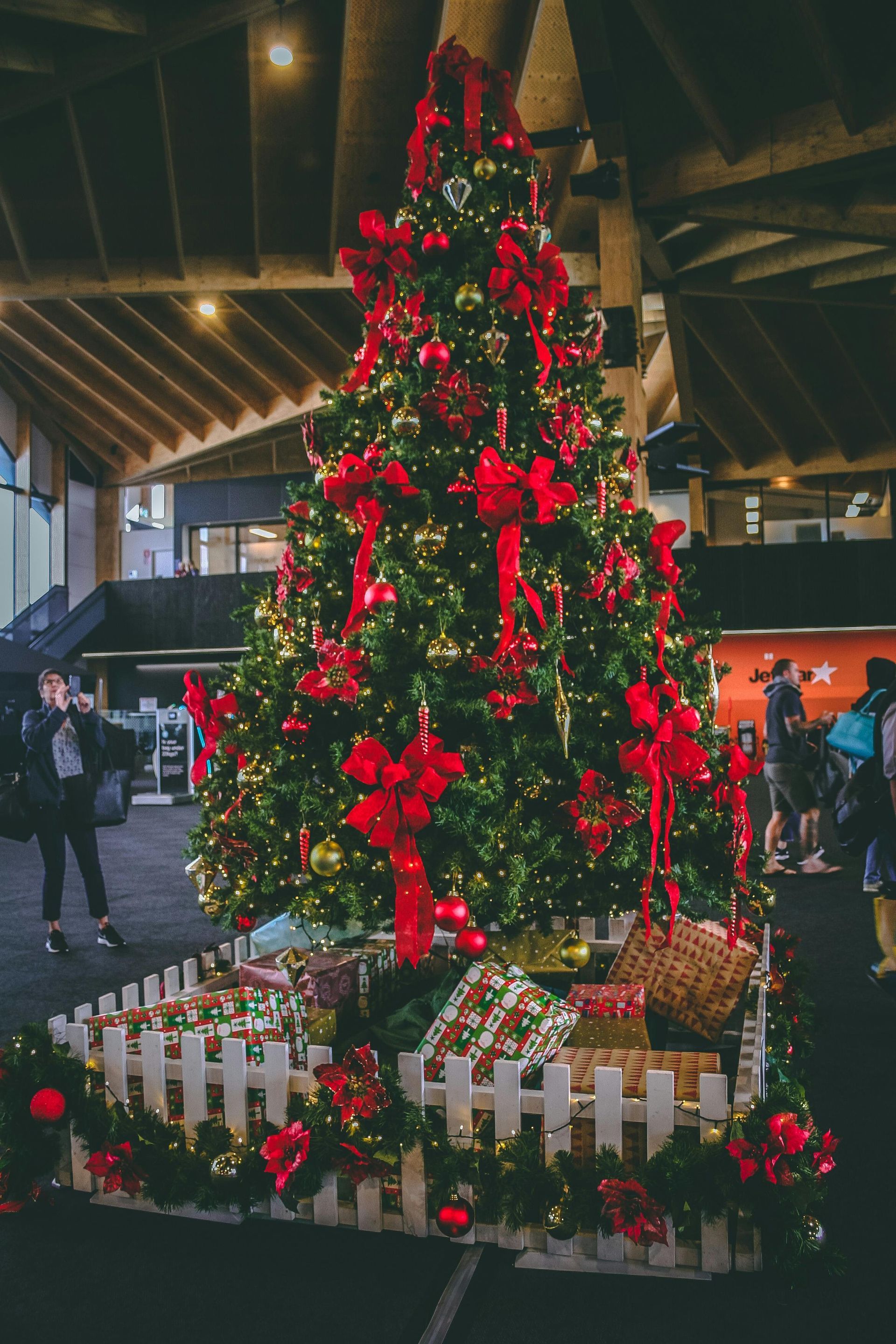 A large christmas tree is decorated with red and gold decorations and gifts.