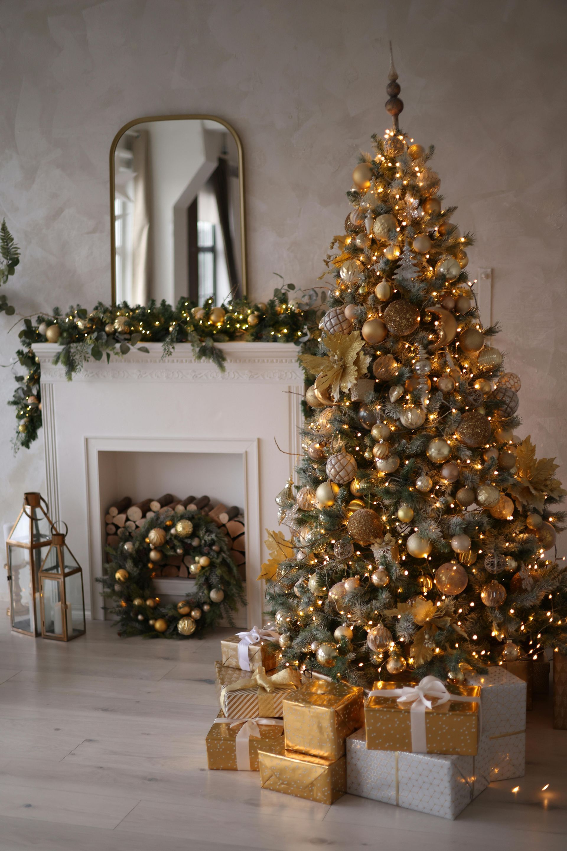 A christmas tree decorated in gold and silver is in a living room next to a fireplace.