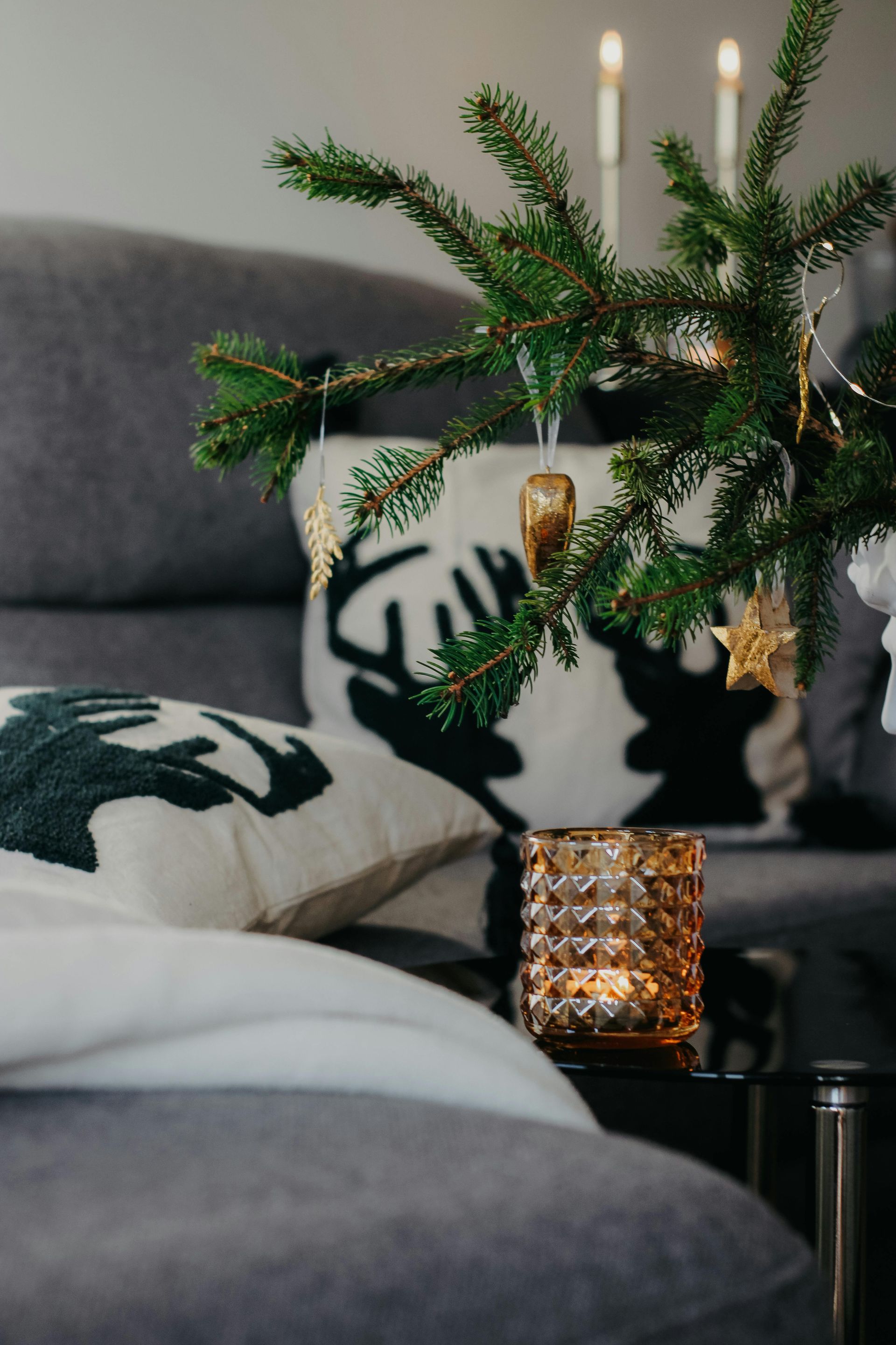 A living room decorated for christmas with a couch , pillows , candles and a christmas tree.
