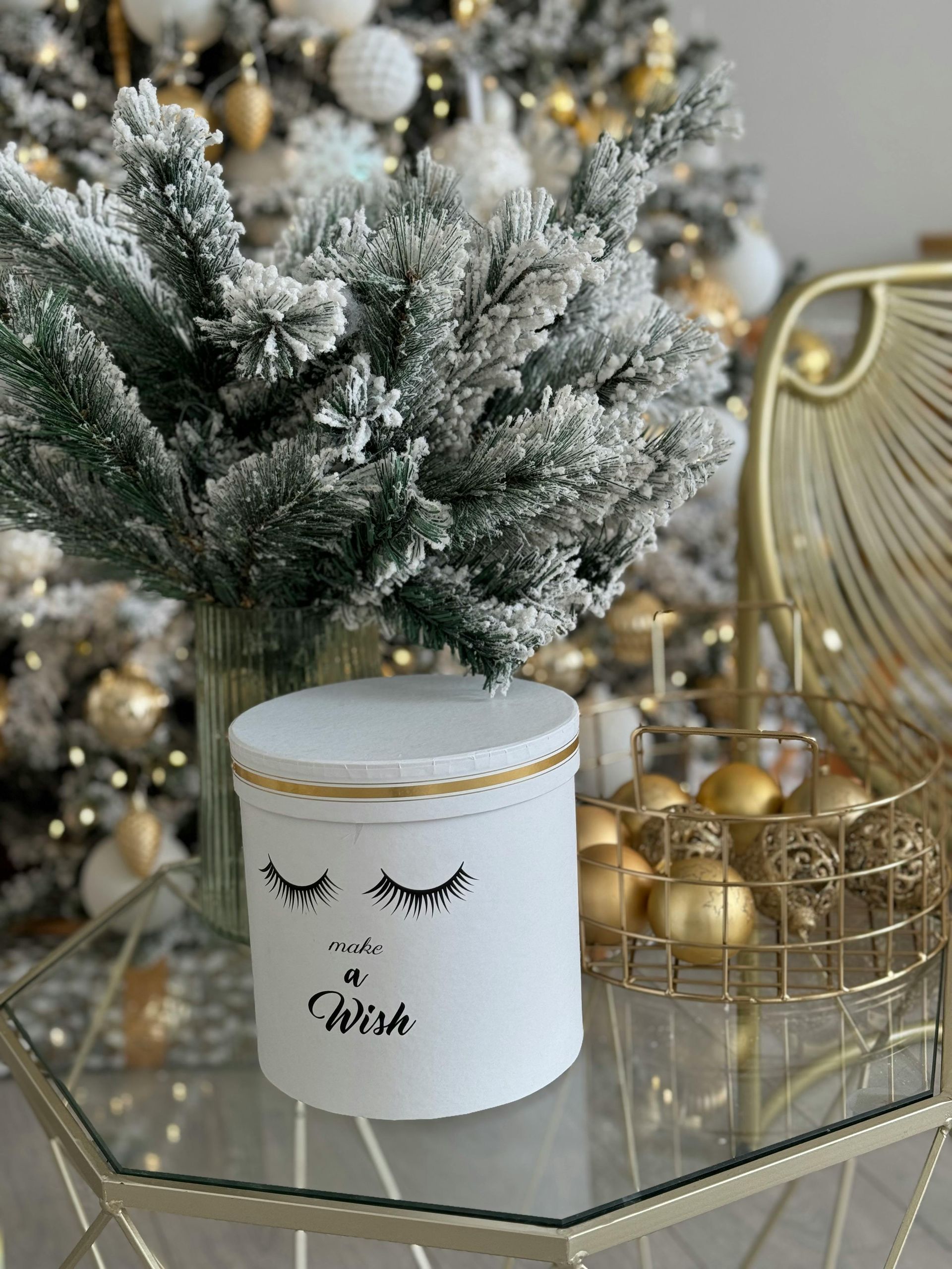 A white box with a face on it is sitting on a glass table in front of a christmas tree.