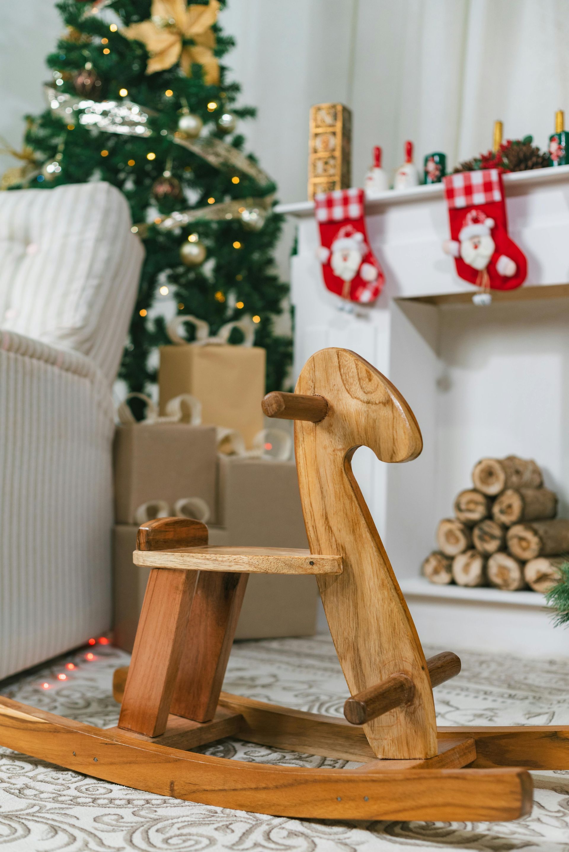 A wooden rocking horse is sitting in front of a christmas tree in a living room.