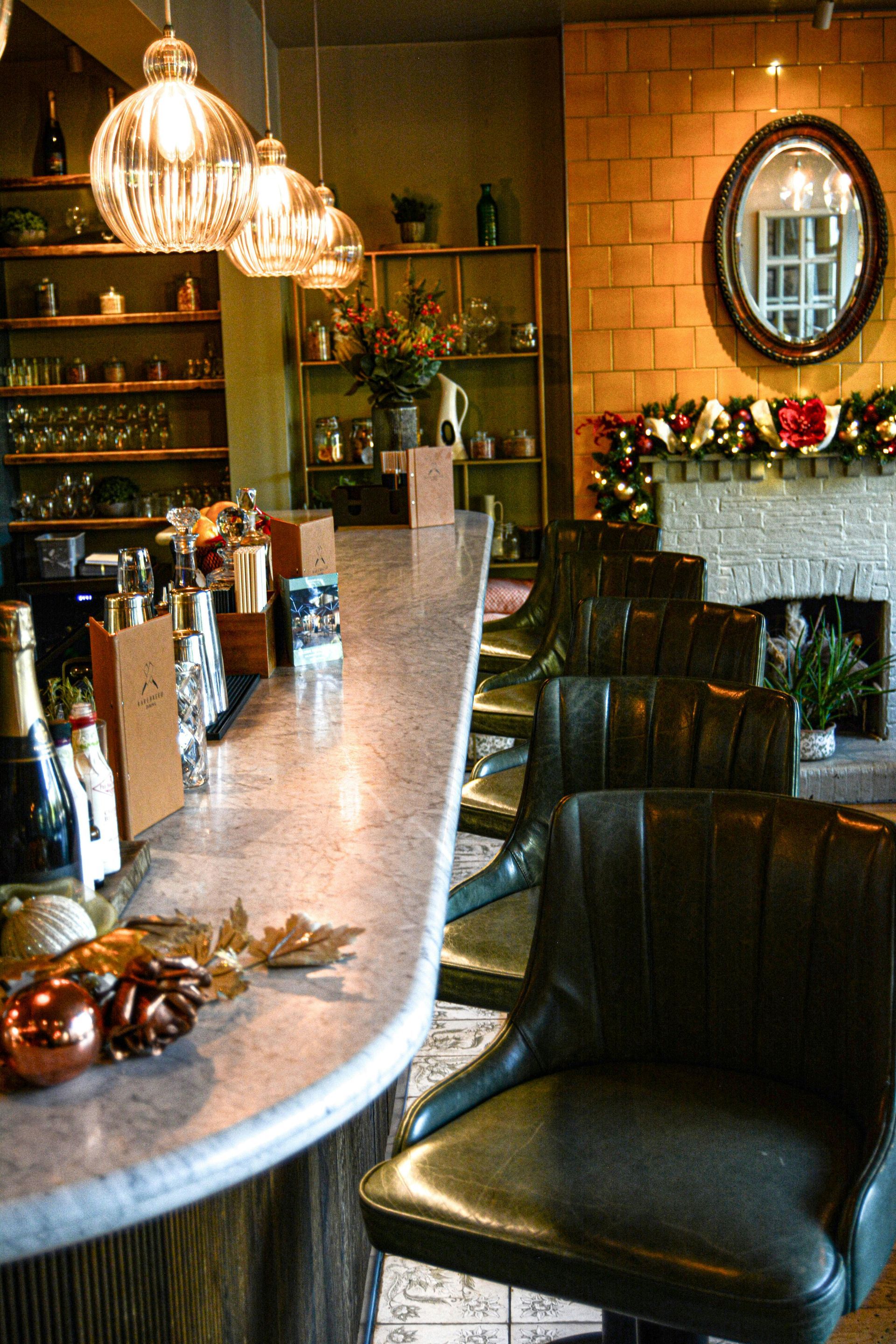 A bar with chairs and a fireplace in the background