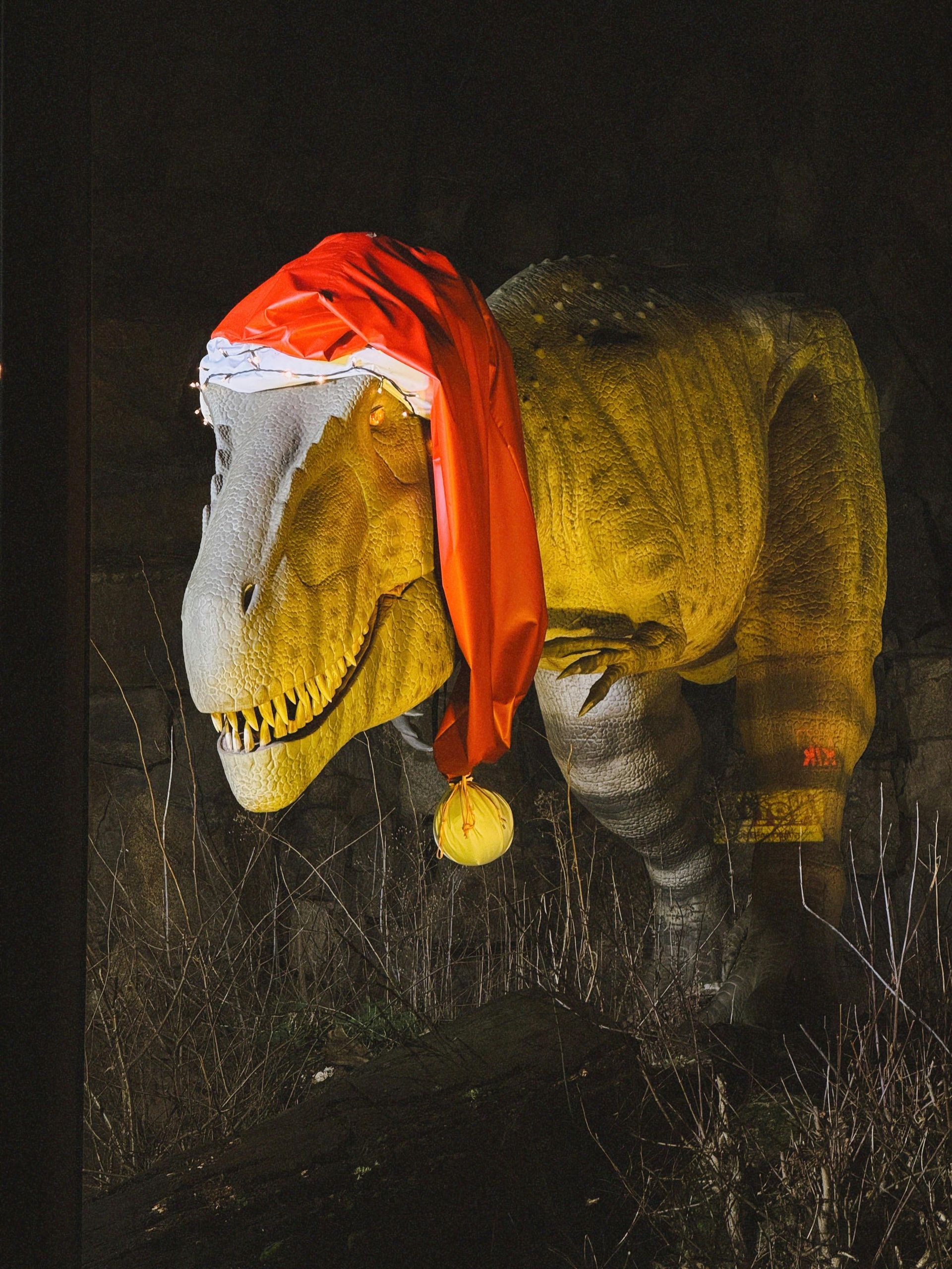 A dinosaur wearing a santa hat is standing in the dark