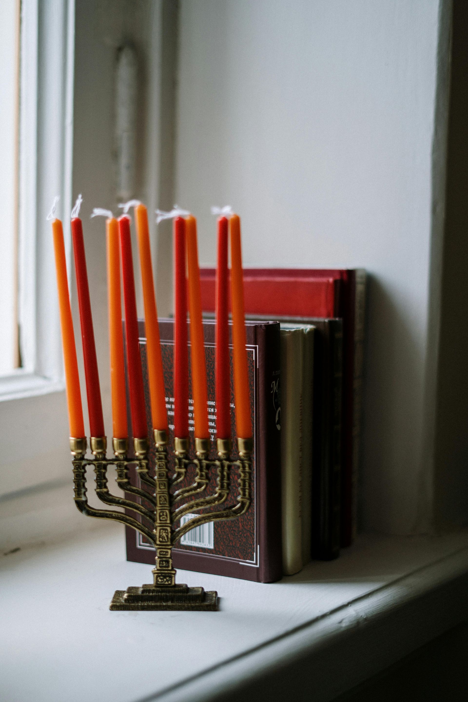 A menorah with orange candles is sitting on a window sill next to a stack of books.