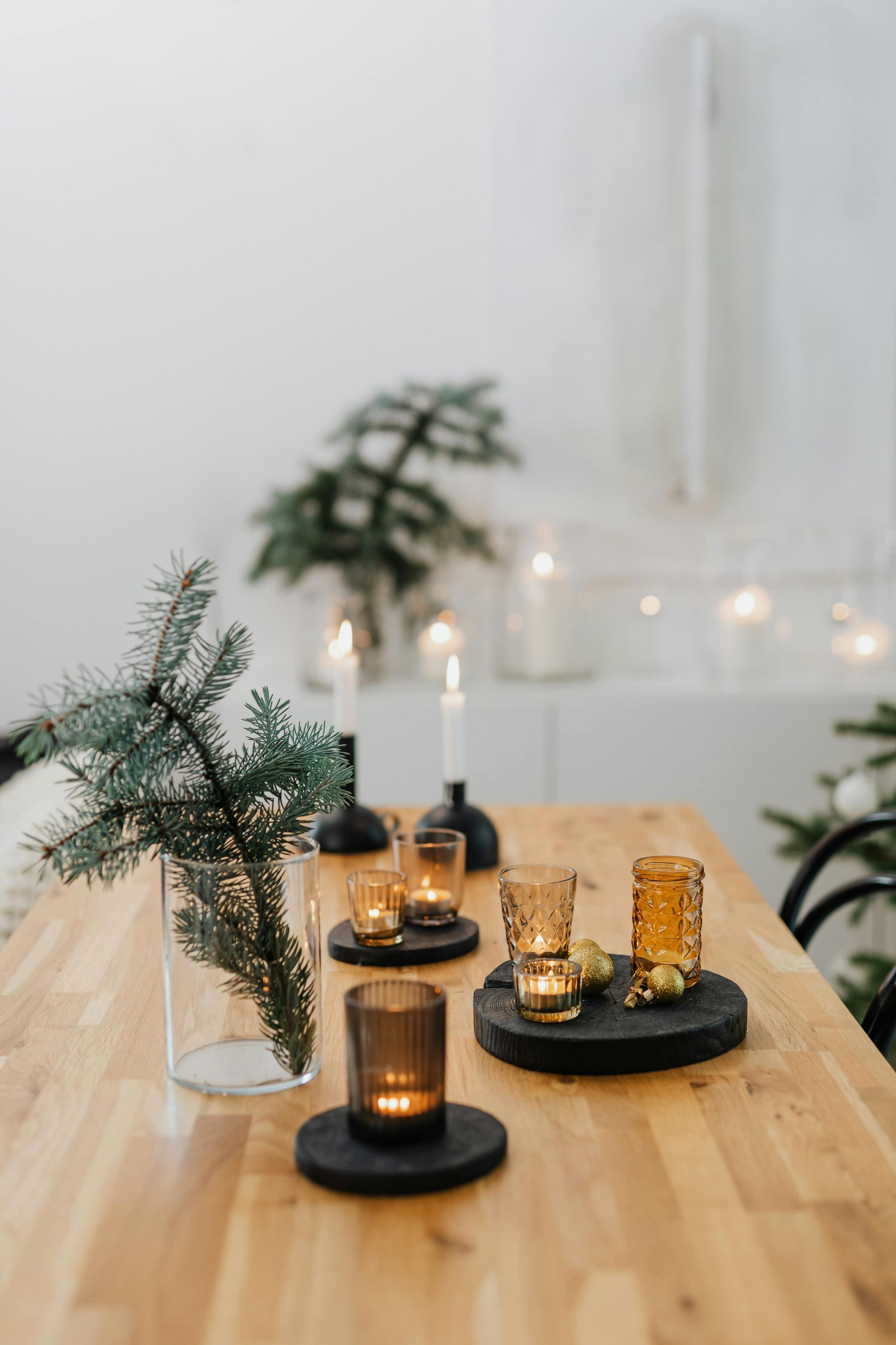 A wooden table with candles and a vase of pine branches on it.