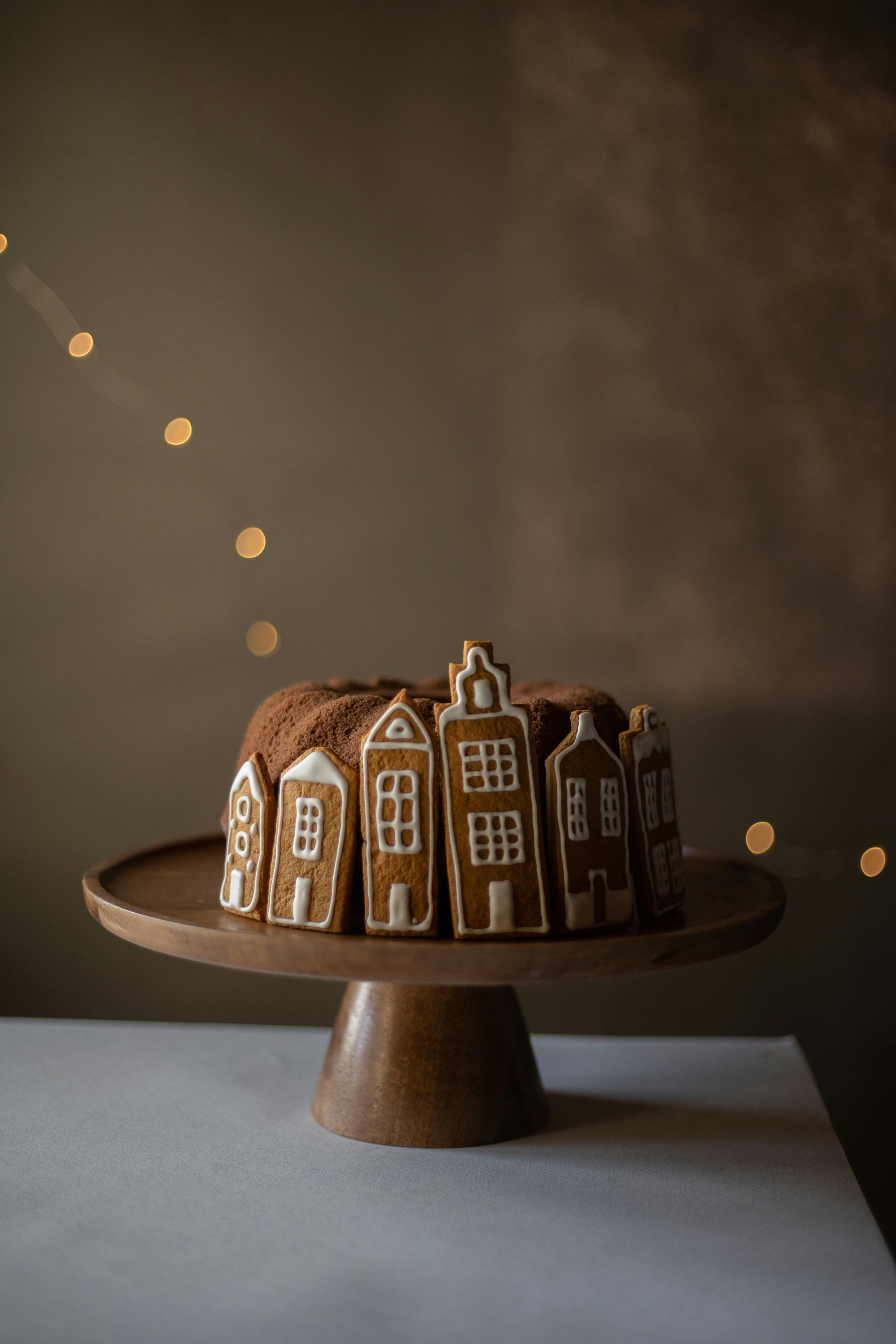 A bundt cake decorated to look like gingerbread houses on a wooden cake stand.