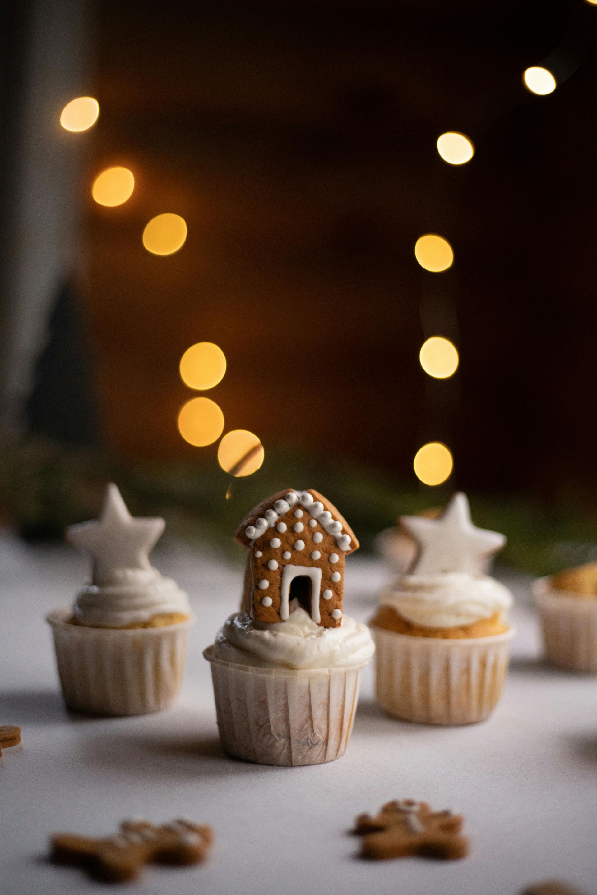 A gingerbread house is on top of a cupcake on a table.