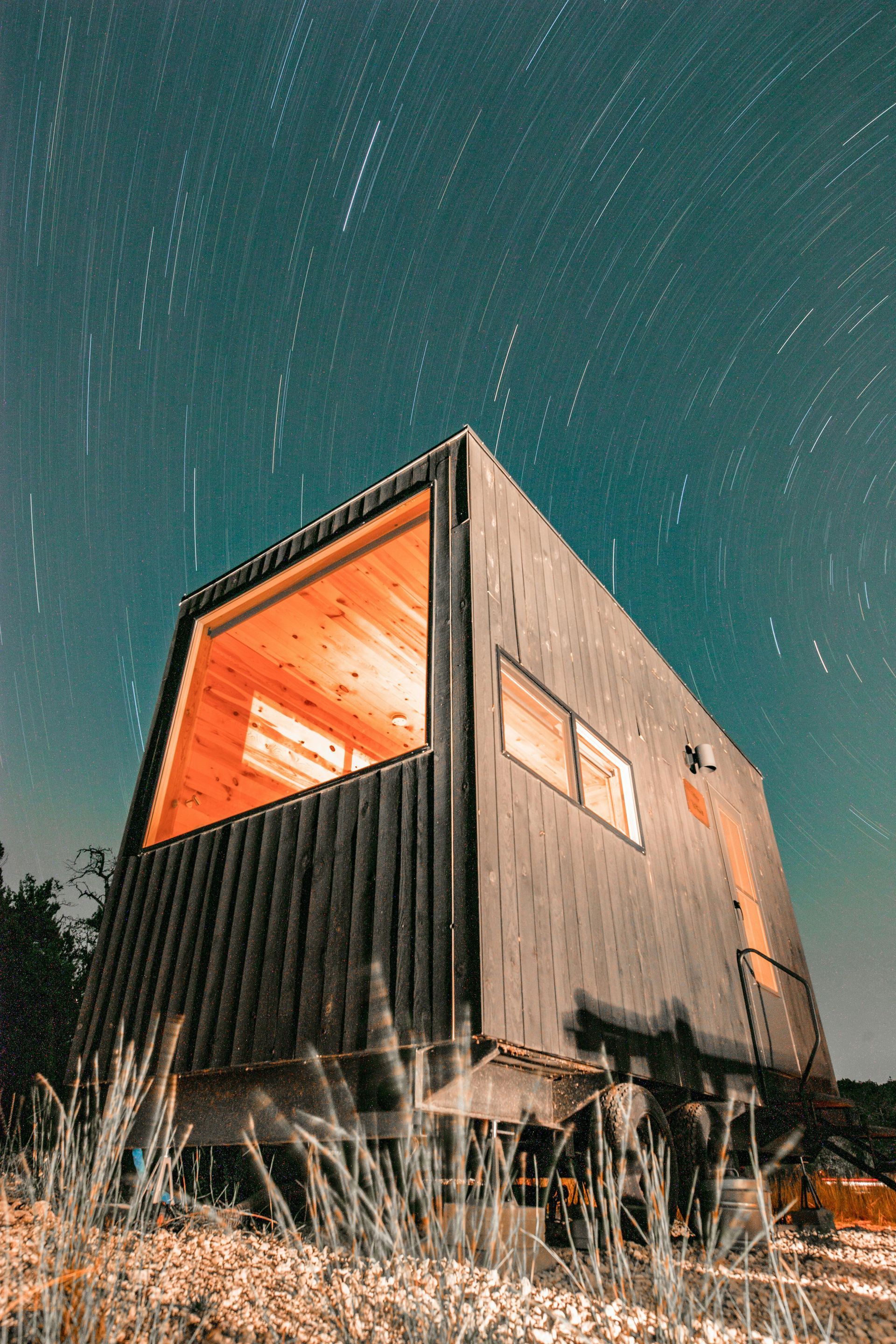 A small house is sitting in the middle of a field under a starry sky.