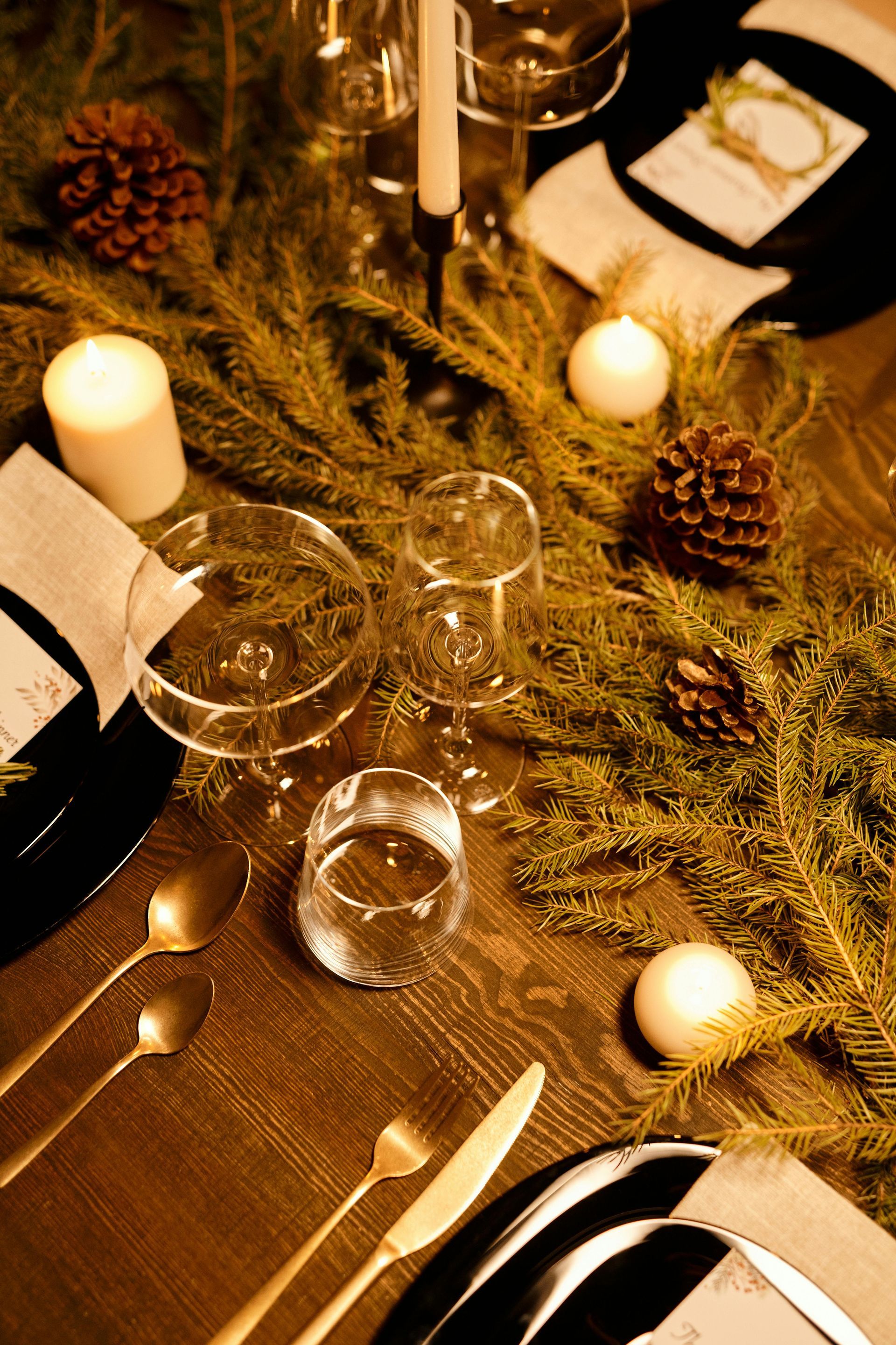A table set for a christmas dinner with candles and pine cones.