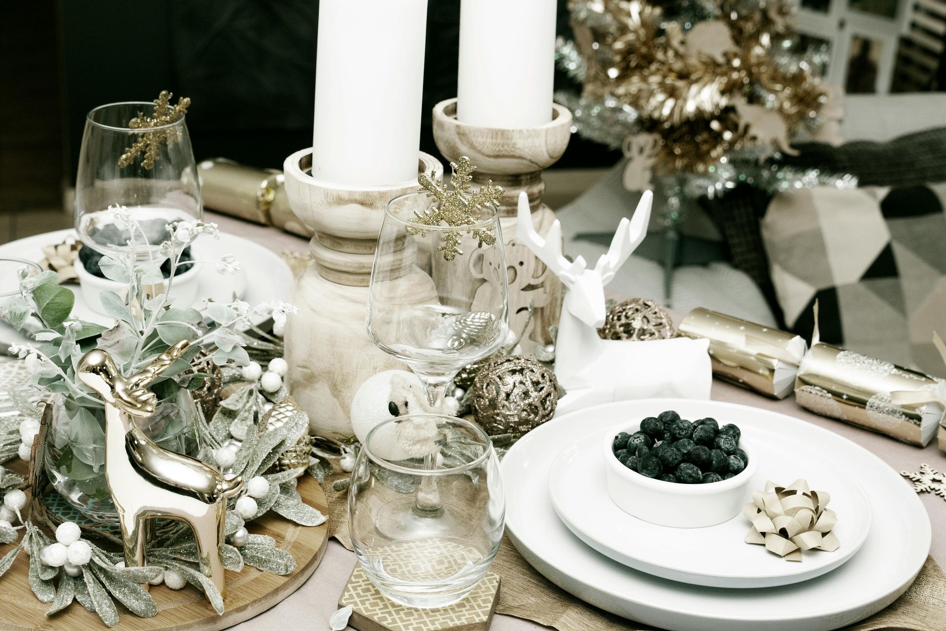 A christmas table setting with plates , candles , glasses and a wreath.