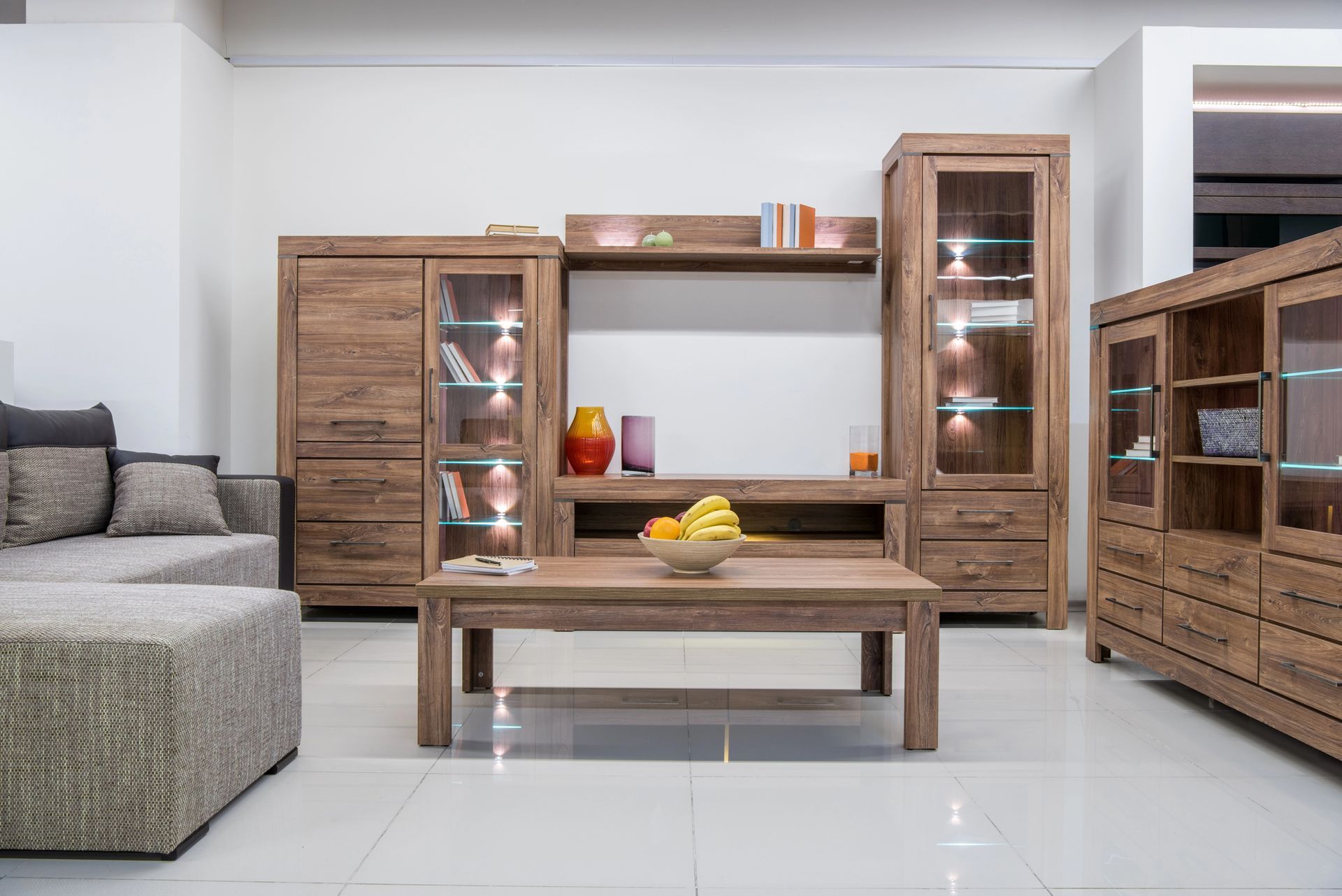 Sala de estar moderna con estanterías de madera, una mesa de centro y un sofá modular gris sobre un suelo de baldosas.