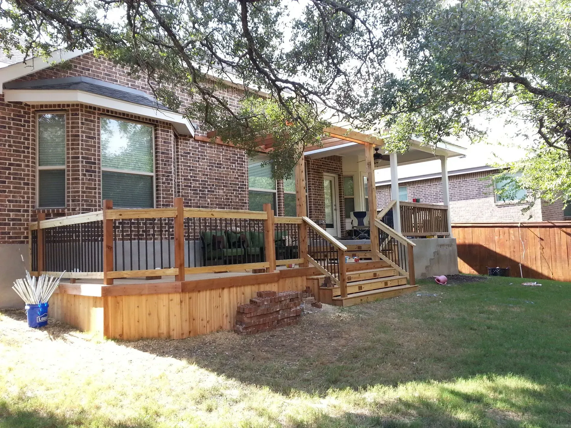 Backyard with new wooden deck and covered porch attached to a brick house.